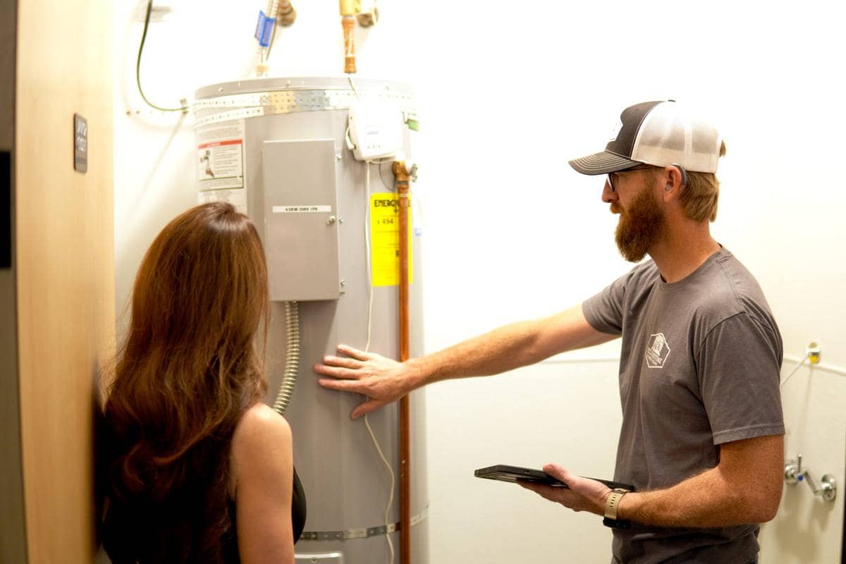A Yellowstone plumber walking a homeowner through a water heater in her garage.